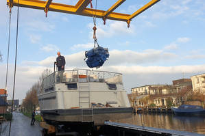 De motor voor de boot Gerda nog hoger hangend in de touwen vlak naast het water van de Pier Christiaansloot