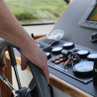 Man met het roer van een motorjacht in handen.